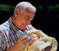 Picture of a grandfather holding his newborn grandson, feeding him a bottle
