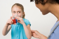 Photo of young girl using asthma inhaler while mother watches
